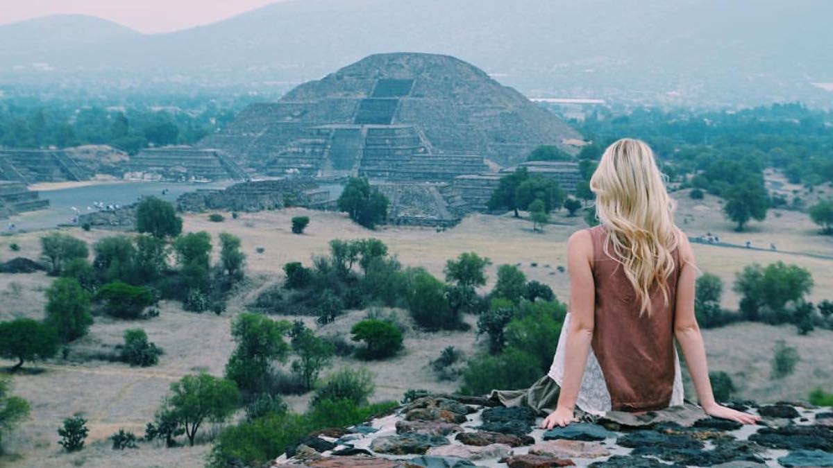 A woman, Cheyanne Herrera, sitting on top of Pyramid of the Sun in Teotihuacan, looking at the Pyramid of the Moon.